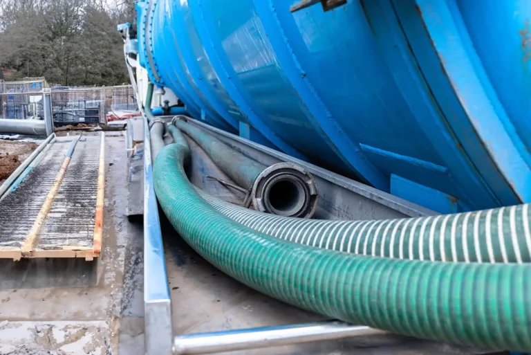 Long 4 inch PVC suction hoses lie next to the tank of the tank truck