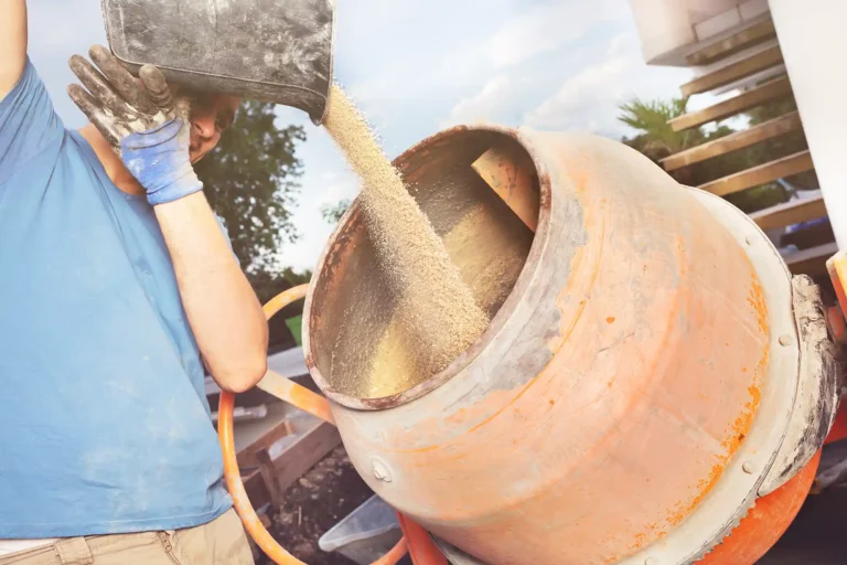 Man adds sand from bucket into cement mixer