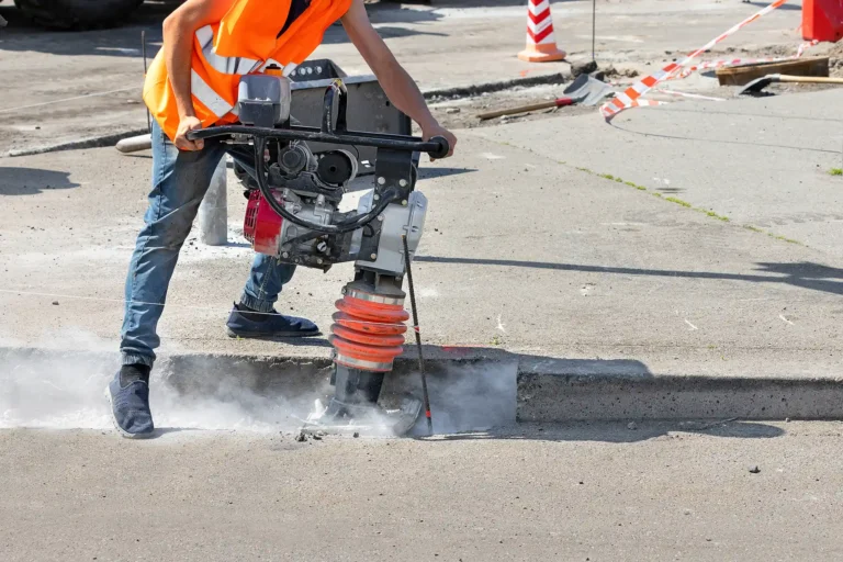 worker compacts the soil with a vibratory rammer in a trench
